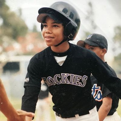 He is wearing a black top with white pant and a black helmet. The shirt spells Rockies.
